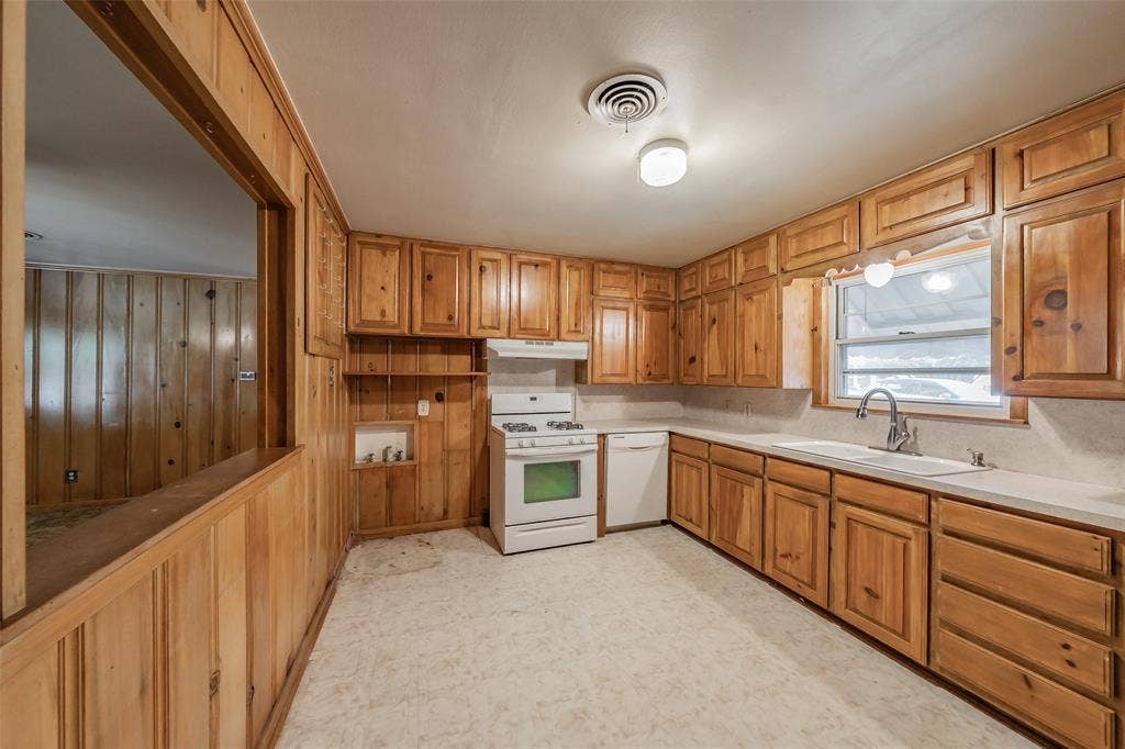 1313 Killian Drive, Arlington, TX 76013 Spacious kitchen featuring rich wood cabinetry throughout, white appliances, light-toned countertops, and a large window overlooking the exterior