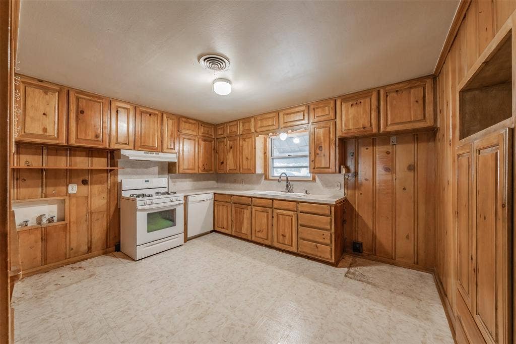 1313 Killian Drive, Arlington, TX 76013 Kitchen featuring extensive wood cabinetry, white appliances, a stainless steel sink with a gooseneck faucet, and a window above the sink