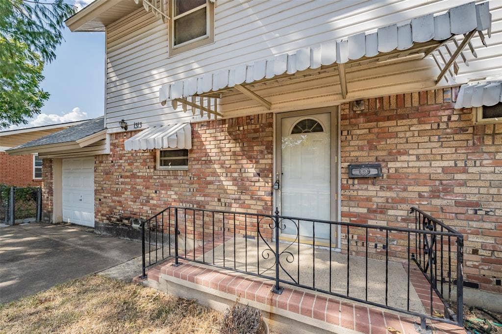 1313 Killian Drive, Arlington, TX 76013 Brick exterior with vinyl siding accents, front entry with storm door, covered porch with wrought iron railing, attached garage with white door, and an exterior awning over the main entry