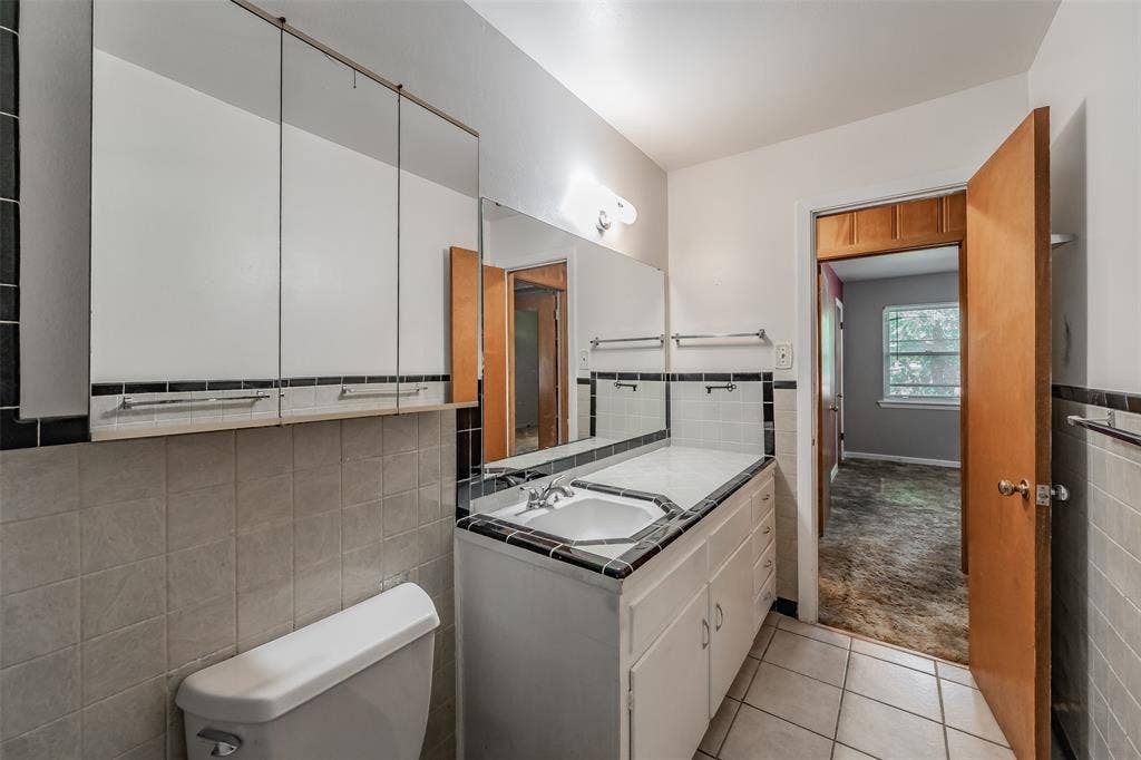 1313 Killian Drive, Arlington, TX 76013 White tile flooring, white vanity with integrated sink, black and white tile accents, mirrored medicine cabinet, and a wooden door