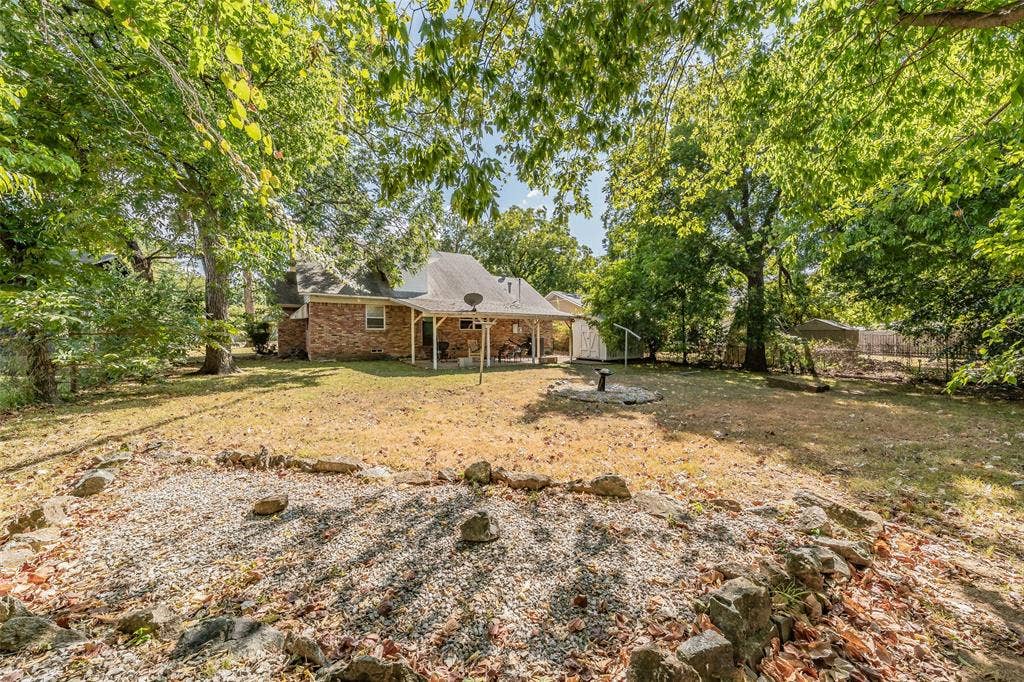 1313 Killian Drive, Arlington, TX 76013 Expansive backyard featuring mature trees, a covered patio, and a dedicated gravel area with rock border