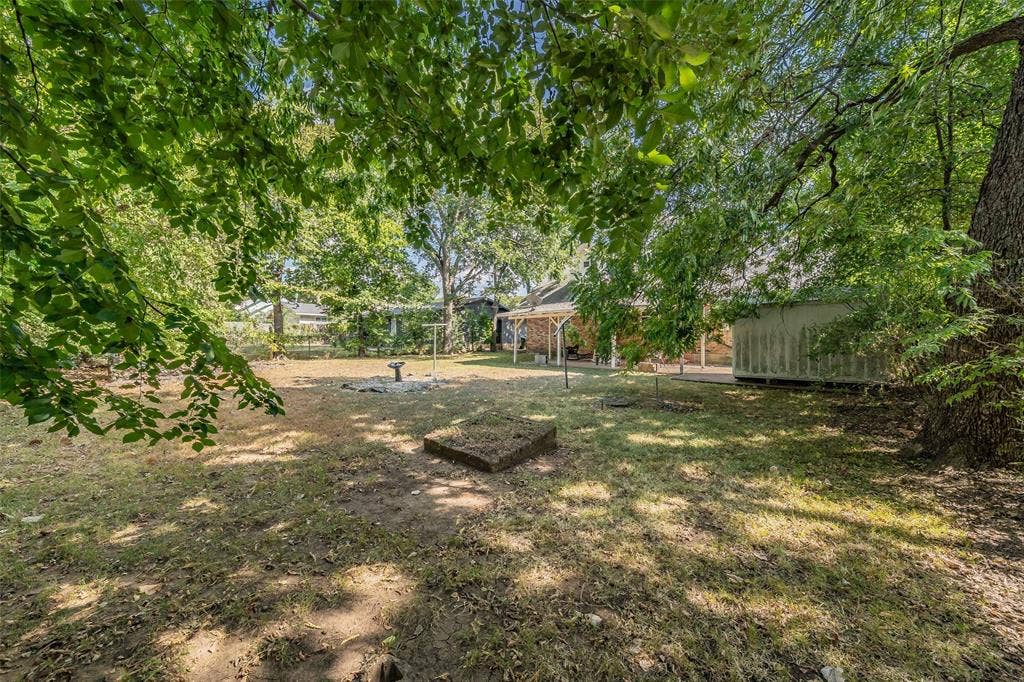 1313 Killian Drive, Arlington, TX 76013 Expansive rear yard featuring mature trees, a covered patio, and a storage structure