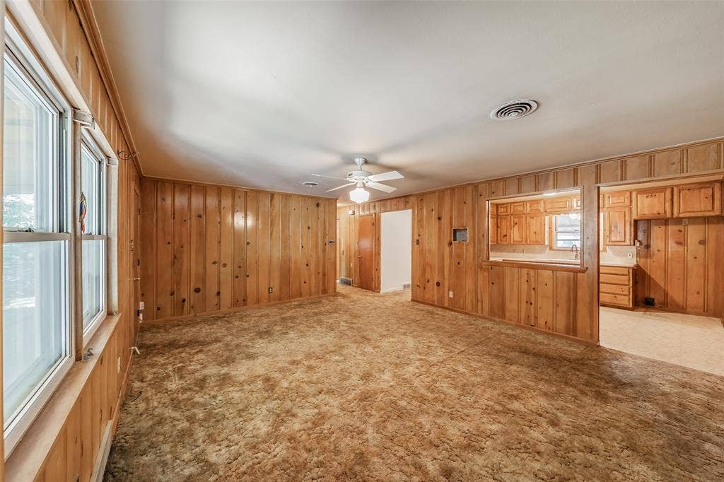 1313 Killian Drive, Arlington, TX 76013 Wood-paneled living space featuring a ceiling fan, multiple windows, and a pass-through opening to a kitchen with wood cabinetry