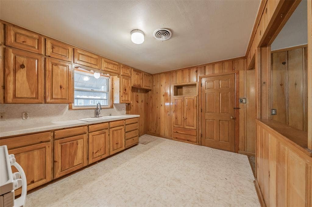 1313 Killian Drive, Arlington, TX 76013 Kitchen featuring extensive wood cabinetry, white countertops, a stainless steel sink, and wall paneling