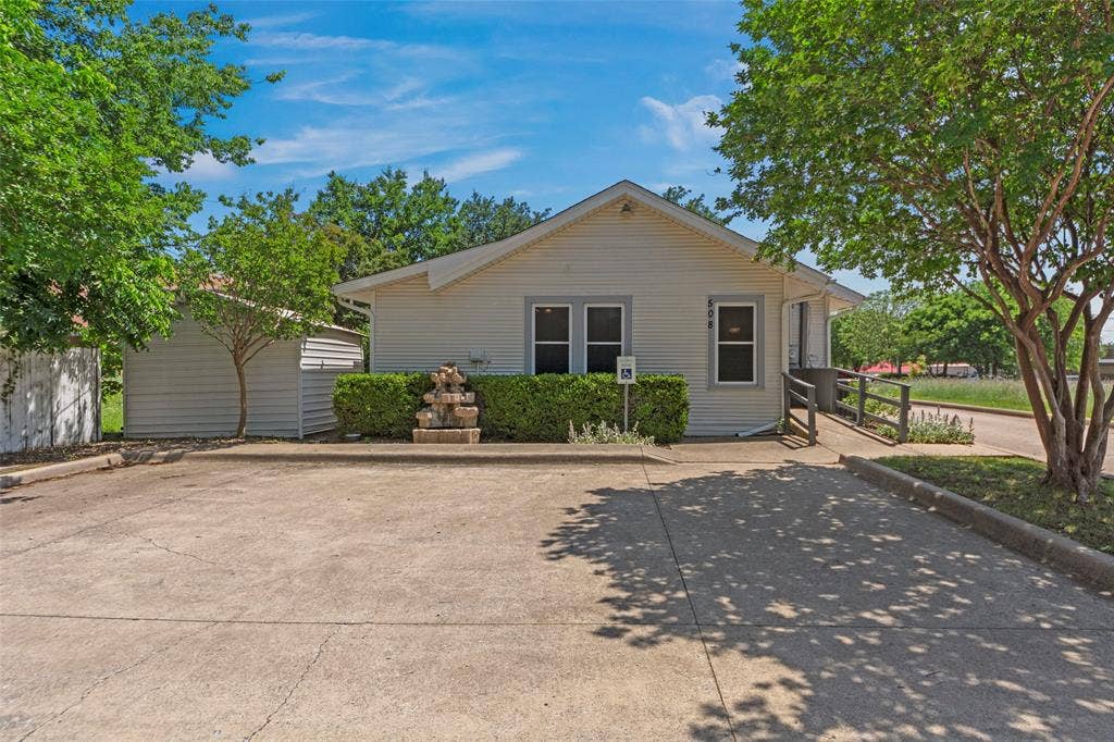 508 W Main Street, Allen, TX 75013 White siding exterior with a gable roof, concrete parking area, and a stone water feature