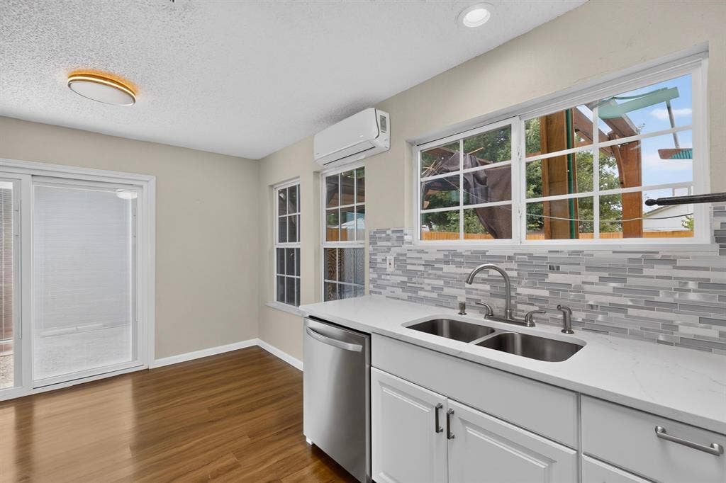 6747 Silver Sage Drive, Fort Worth, TX 76137 Sliding glass door, wood-finish flooring, white cabinetry, stainless steel double-basin sink, and a multi-tone tile backsplash
