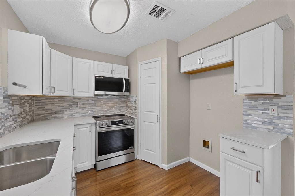 6747 Silver Sage Drive, Fort Worth, TX 76137 White cabinetry, stainless steel appliances, patterned tile backsplash, wood-finish flooring, and a double basin sink