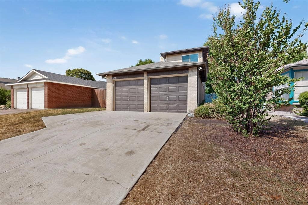 6747 Silver Sage Drive, Fort Worth, TX 76137 Two-car garage with panel doors, concrete driveway, and mature landscaping