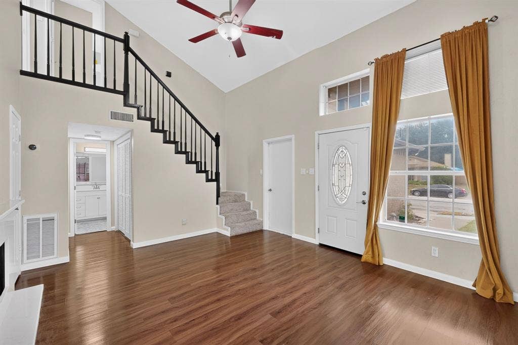 6747 Silver Sage Drive, Fort Worth, TX 76137 Vaulted ceiling with a ceiling fan, wood-finish flooring, staircase with black wrought iron spindles, white entry door with leaded glass insert, and a transom window