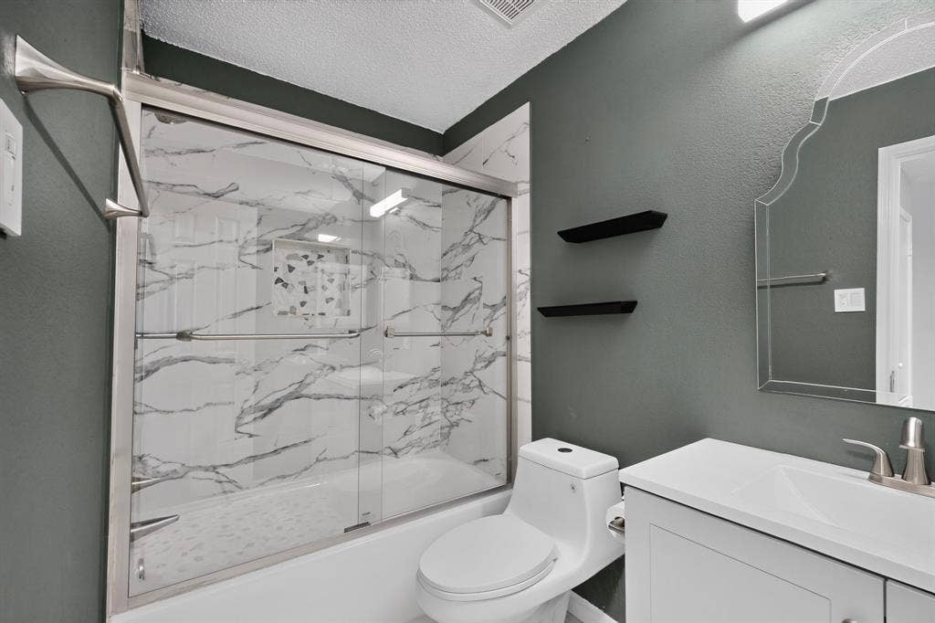 6747 Silver Sage Drive, Fort Worth, TX 76137 Tub with sliding glass enclosure, white marble-look surround, white vanity with integrated sink, and decorative mirror
