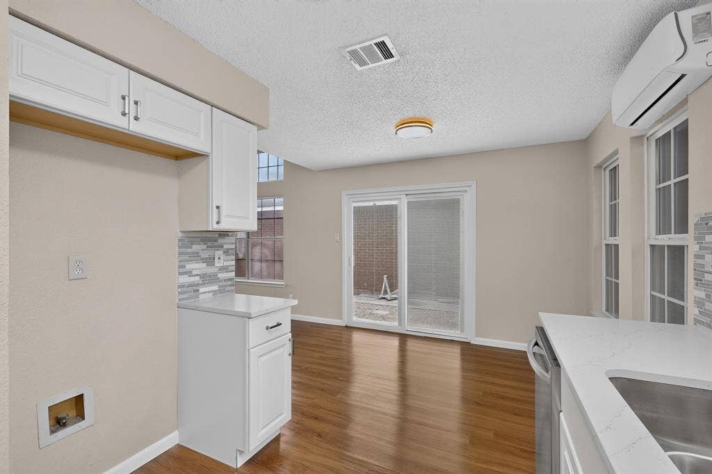 6747 Silver Sage Drive, Fort Worth, TX 76137 White cabinetry with dark hardware, stone-finish countertops, wood-finish flooring, sliding glass door, and multiple windows