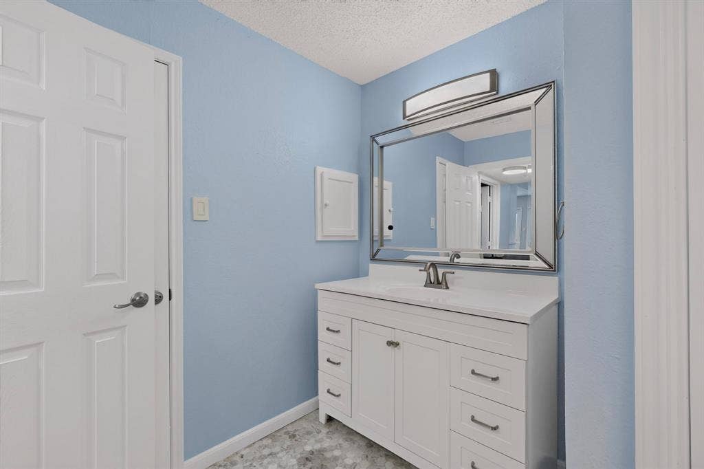 6747 Silver Sage Drive, Fort Worth, TX 76137 White vanity cabinet with integrated sink, rectangular framed mirror, and chrome-finish fixtures