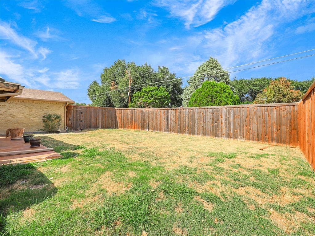 Spacious backyard featuring a wood deck, wood privacy fencing, and mature perimeter trees