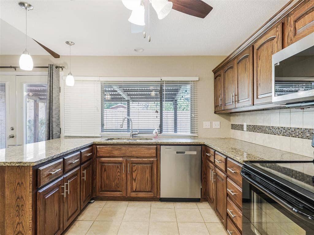 Kitchen featuring wood cabinetry, granite countertops, tile flooring, stainless steel dishwasher, and pendant lighting