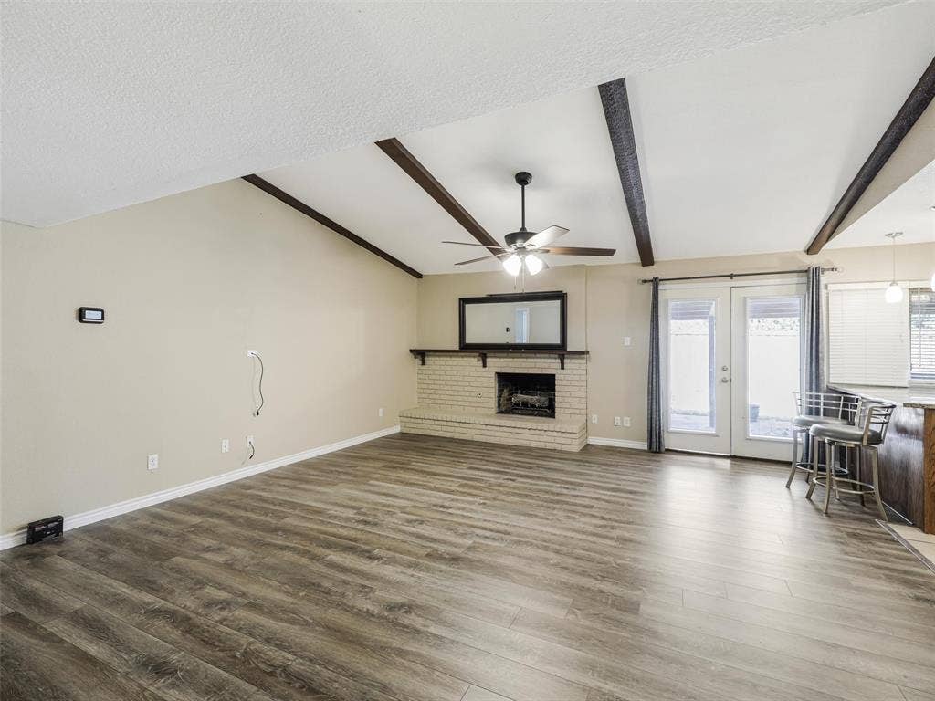 Vaulted ceiling with exposed beams, brick fireplace with mantel, wood-finish flooring, and double glass panel doors