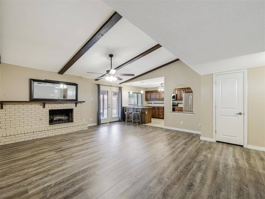 Vaulted ceiling with exposed wood beams, brick fireplace, wood-finish flooring, and French doors
