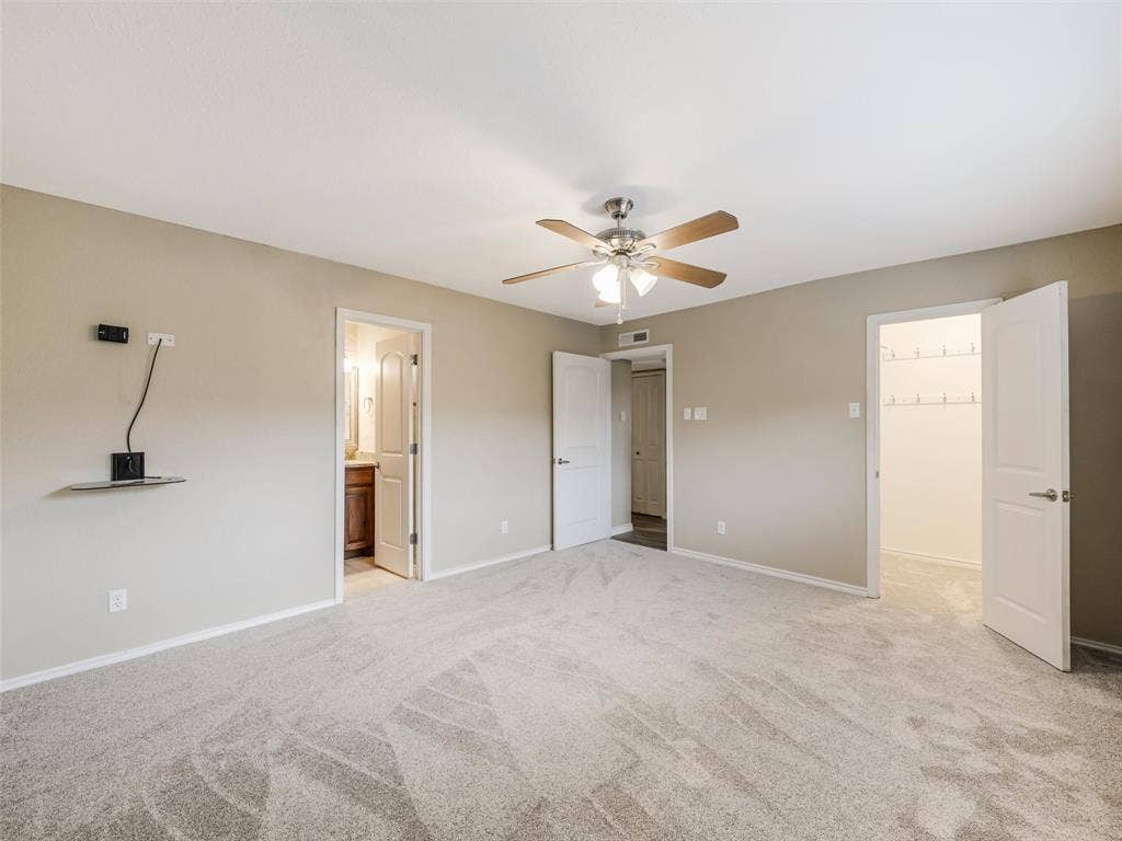 Spacious room with light neutral wall tones, gray patterned carpet, ceiling fan with integrated lighting, and multiple white panel doors