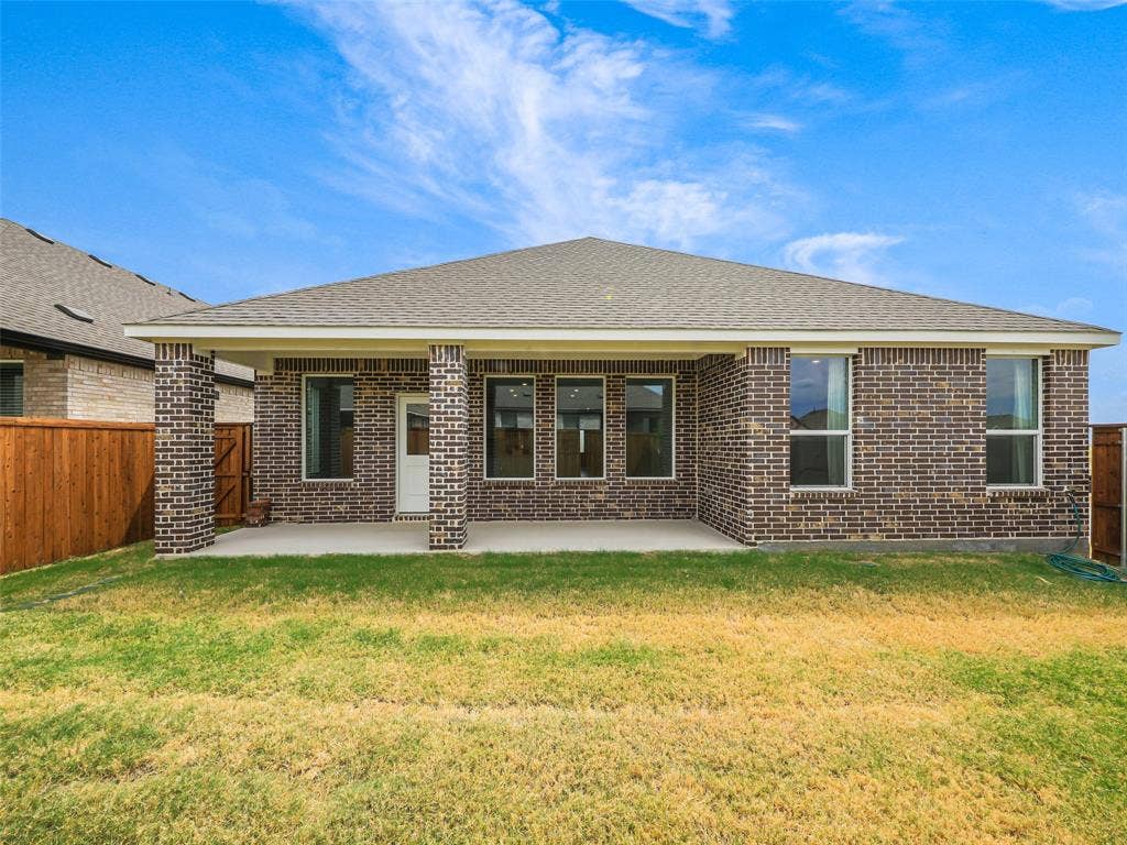2517 Greenbelt Road, Celina, TX 75009 Rear exterior featuring a covered patio, dark brick facade, multiple windows, and a wood privacy fence