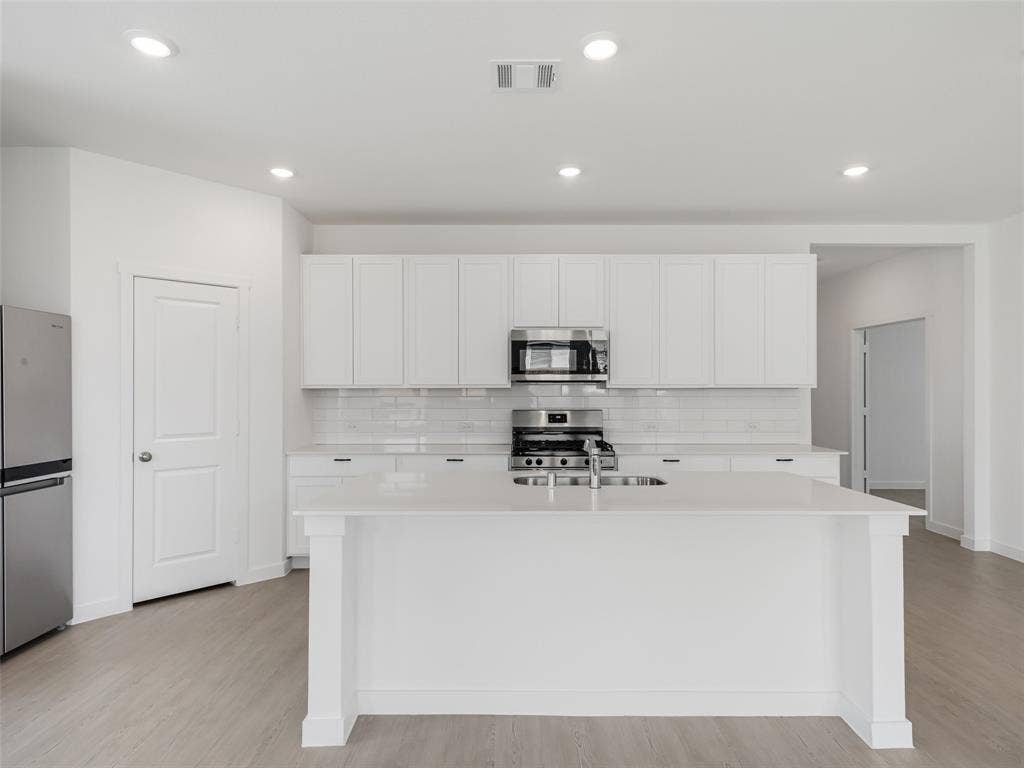 2517 Greenbelt Road, Celina, TX 75009 Contemporary kitchen featuring white cabinetry, a large center island, stainless steel appliances, recessed lighting, and wood-finish flooring