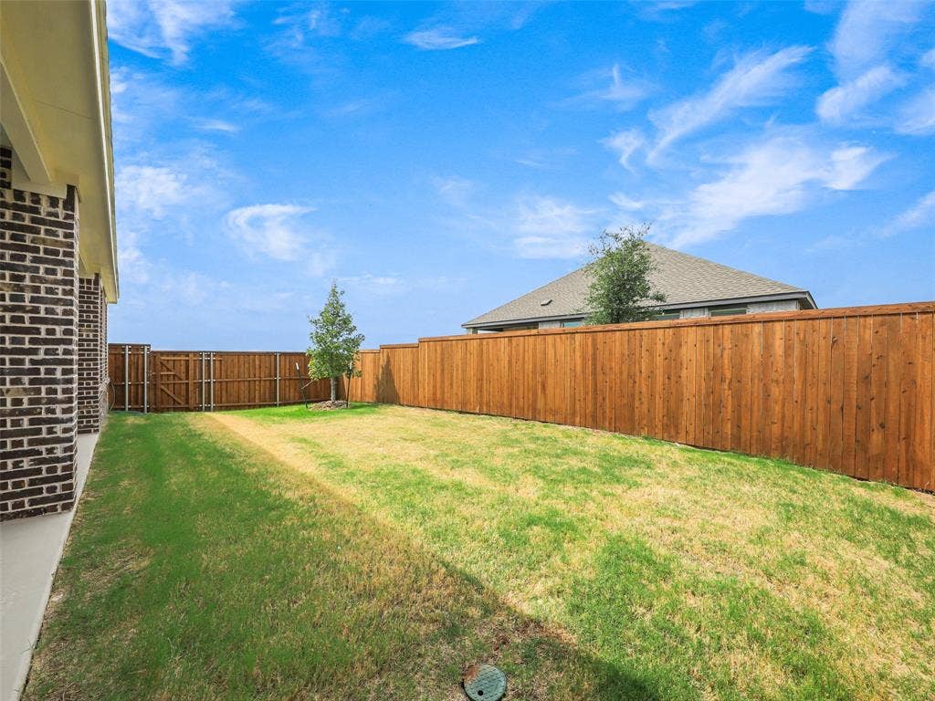 2517 Greenbelt Road, Celina, TX 75009 Expansive backyard featuring a manicured lawn, wood fencing, and a brick-clad exterior wall