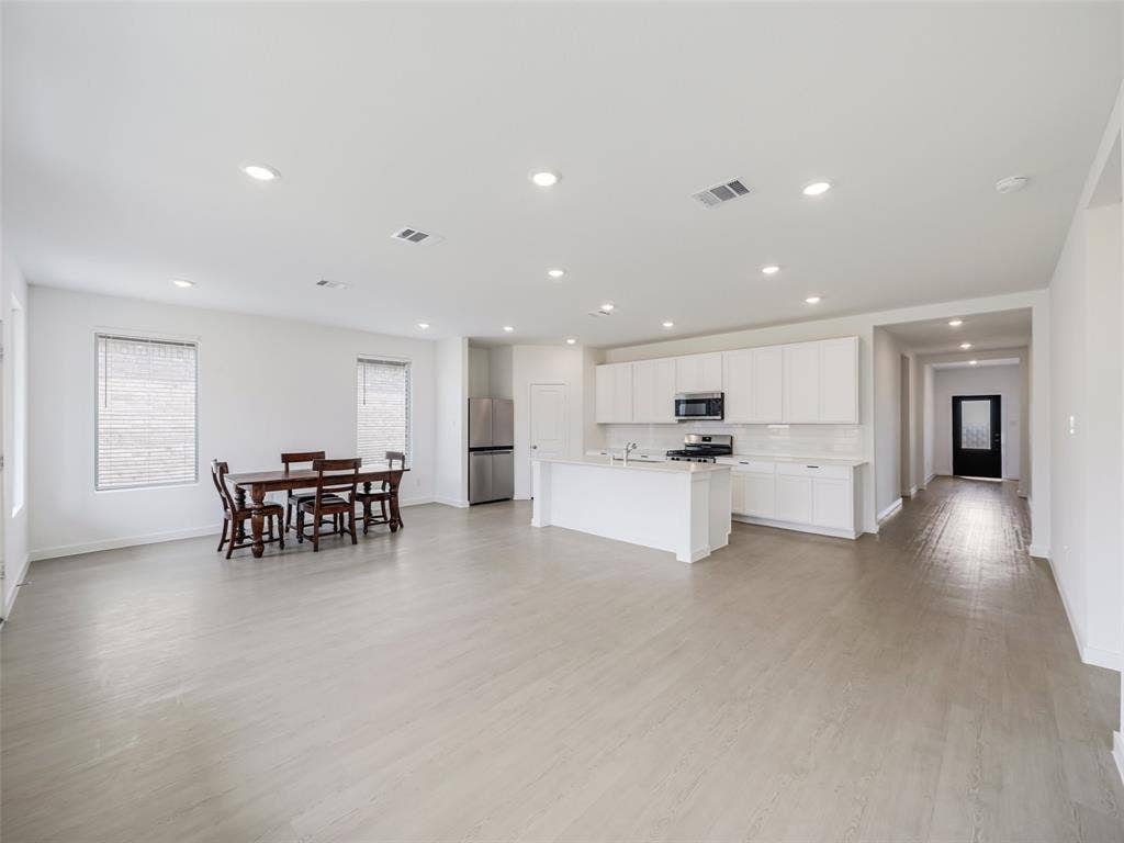 2517 Greenbelt Road, Celina, TX 75009 Open-concept living and kitchen area featuring recessed ceiling lighting, white cabinetry with stainless steel appliances, wood-finish flooring throughout, and abundant natural light from multiple windows