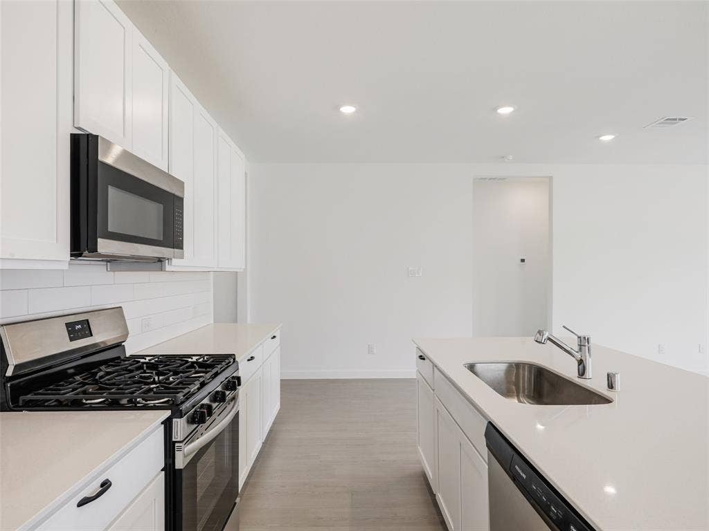 2517 Greenbelt Road, Celina, TX 75009 White cabinetry with black hardware, stainless steel appliances, solid surface countertops, light wood-finish flooring, and recessed ceiling lighting
