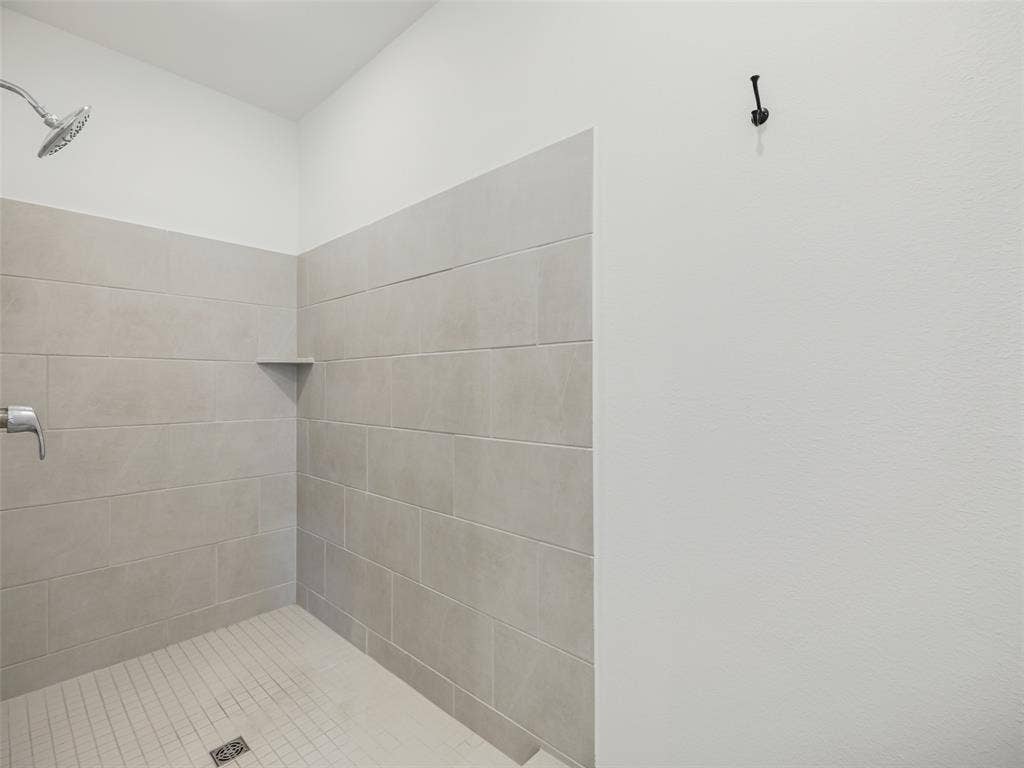 2517 Greenbelt Road, Celina, TX 75009 Shower enclosure featuring light-colored tile walls, a built-in corner shelf, and a textured white wall