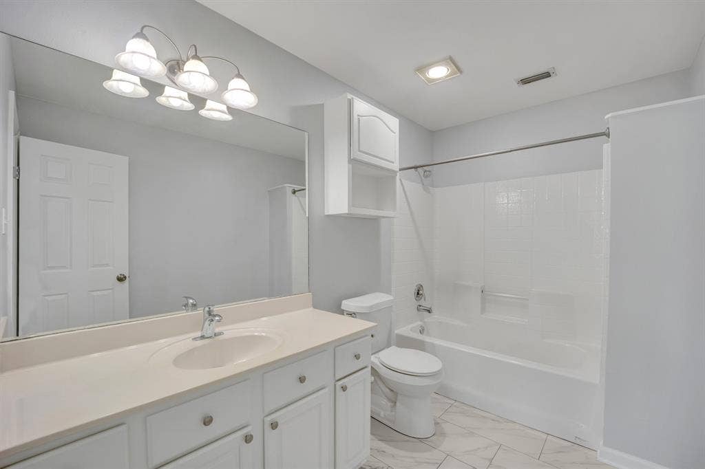 Bathroom featuring a vanity with an integrated sink, a large wall-mounted mirror, a tub/shower combination, and tiled flooring