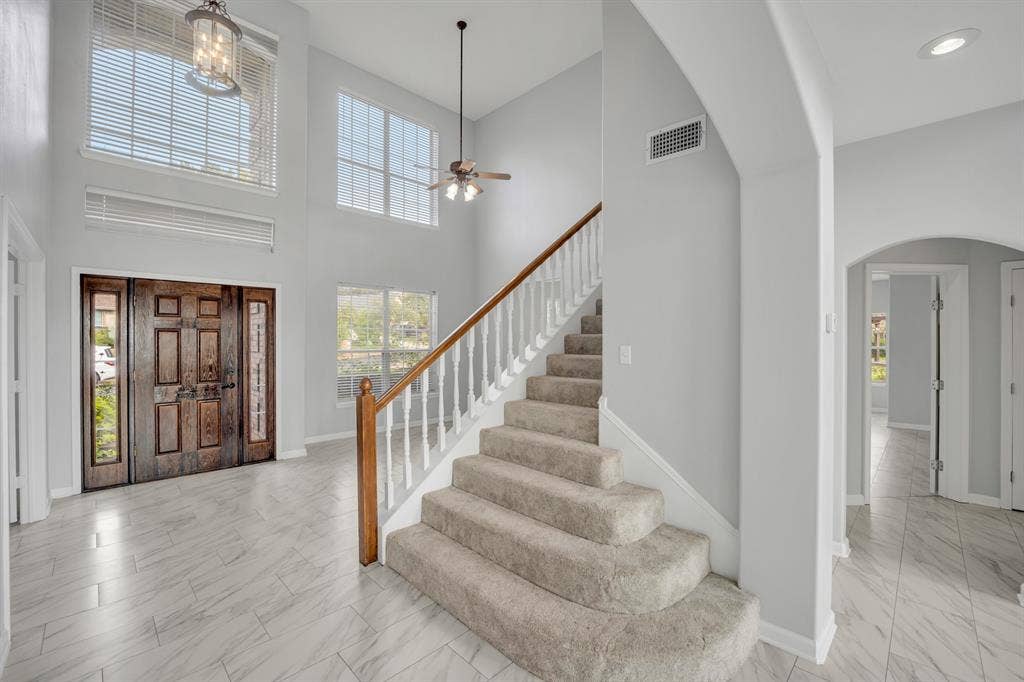 Expansive foyer with a two-story ceiling, natural wood double entry doors with integrated sidelights, and light-toned tile flooring