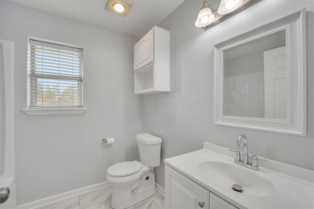 Bathroom featuring a single window, white vanity with integrated sink, chrome faucet, wall-mounted mirror, and white storage cabinetry