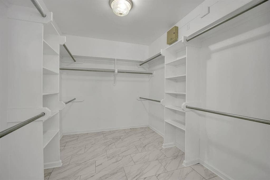 Expansive walk-in closet featuring built-in shelving, multiple hanging rods, and patterned tile flooring