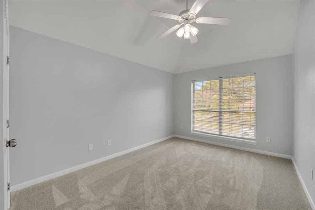 Vaulted ceiling, ceiling fan with light fixture, gray wall paint, window with blinds, and light-toned carpet flooring