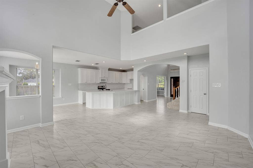 Two-story vaulted ceilings with a ceiling fan, arched doorways, white tile flooring, recessed lighting, and a kitchen with white cabinetry and a subway tile backsplash