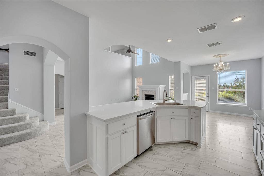 Central kitchen island with a stainless steel sink, white cabinetry, and a built-in dishwasher