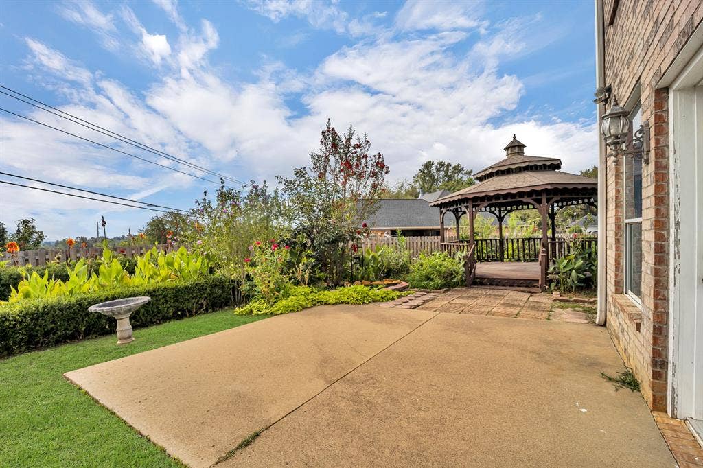 Expansive patio featuring a built-in gazebo, manicured lawn, and mature landscaping