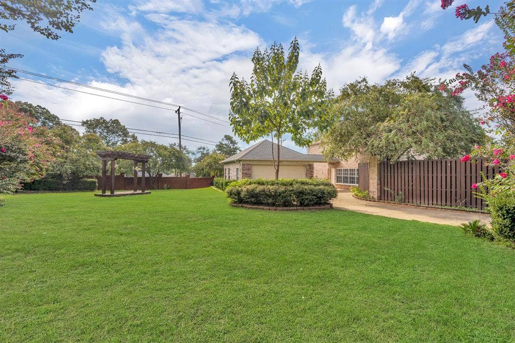 Expansive green lawn with a pergola, mature trees, and a wooden privacy fence