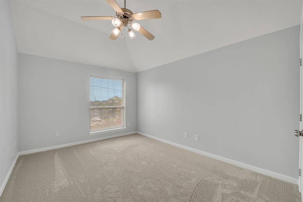 Vaulted ceiling with an attached ceiling fan, neutral wall paint, and carpet flooring