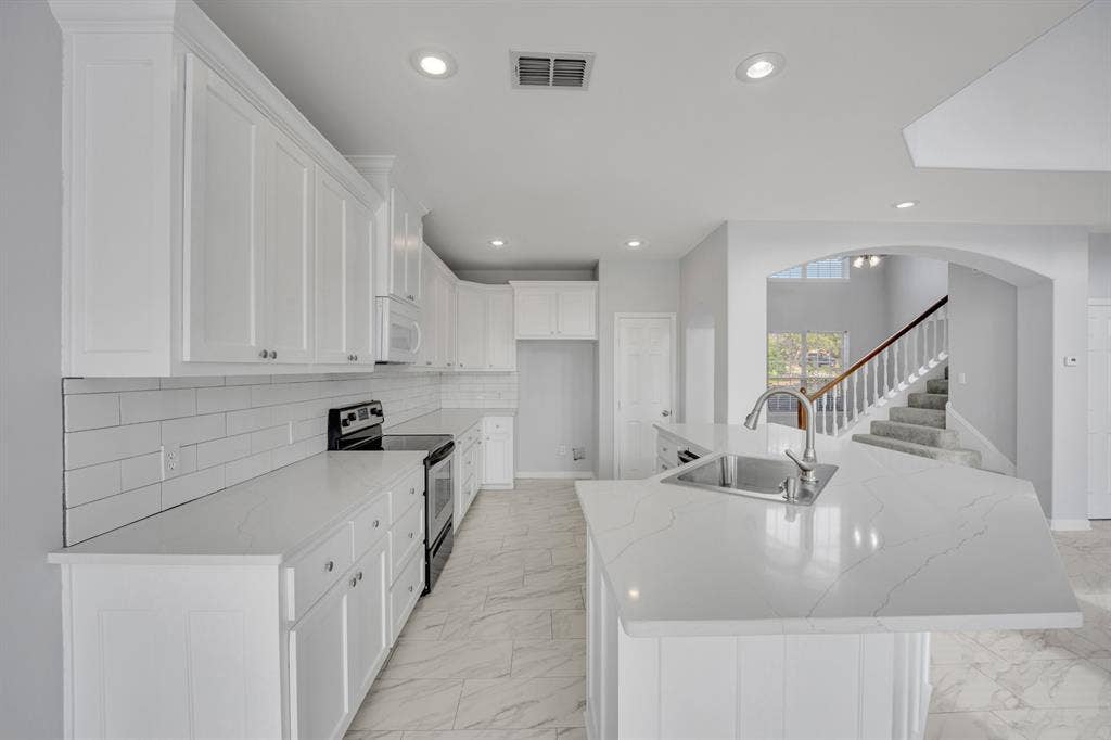 Kitchen featuring white shaker-style cabinetry, subway tile backsplash, white countertops, and a center island with an undermount sink