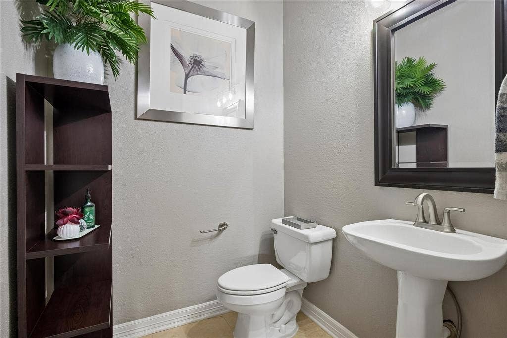 7525 Cedar Elm Drive, Irving, TX 75063 Pedestal sink with a brushed nickel faucet, large framed mirror, wood-finish shelving unit, and tile flooring