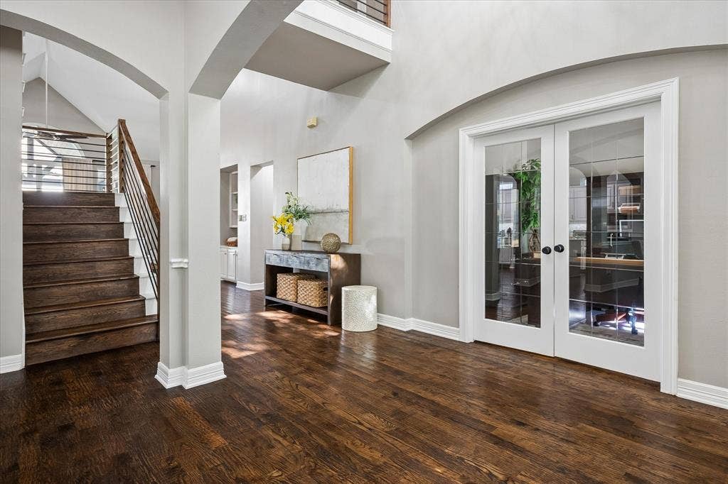 7525 Cedar Elm Drive, Irving, TX 75063 Hardwood flooring, arched doorways, a staircase with metal and wood-finish railings, and white-framed glass French doors