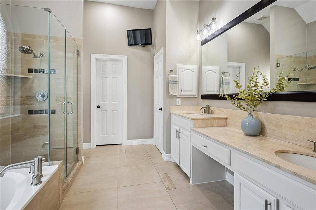 7525 Cedar Elm Drive, Irving, TX 75063 Spacious bathroom featuring a double vanity with stone countertops, white cabinetry, a large frameless glass shower enclosure, and a built-in bathtub
