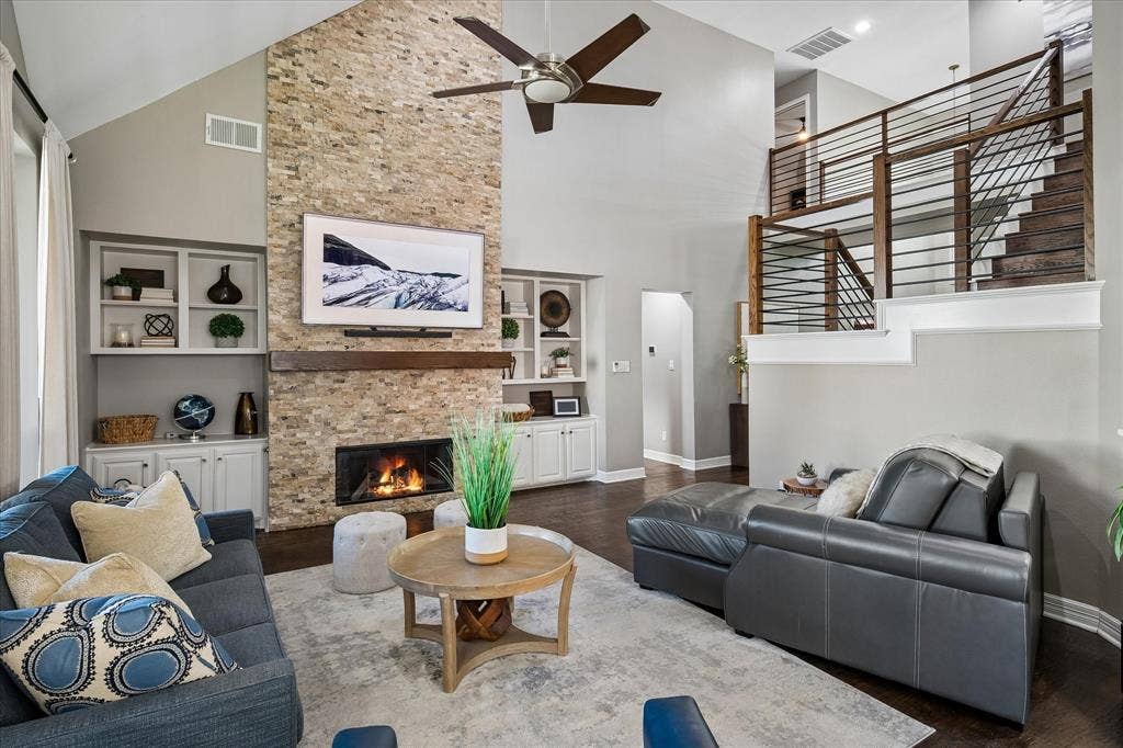 7525 Cedar Elm Drive, Irving, TX 75063 Vaulted ceiling with a ceiling fan, stone-clad fireplace with wood mantel, built-in shelving, wood-finish flooring, and a modern staircase with wood and metal railing