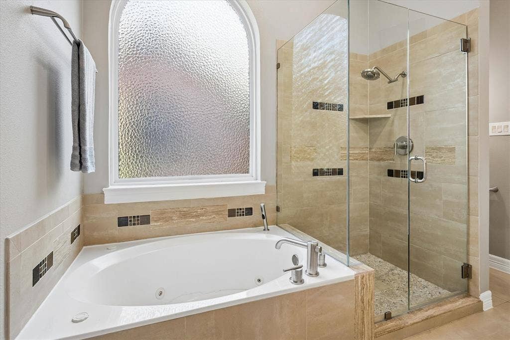 7525 Cedar Elm Drive, Irving, TX 75063 Corner soaking tub with polished chrome fixtures, framed by an arched privacy window