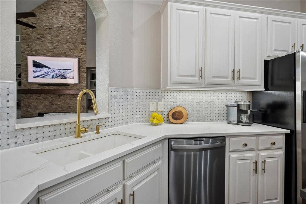 7525 Cedar Elm Drive, Irving, TX 75063 White cabinetry with gold-tone hardware, white countertop surfaces, and a mosaic tile backsplash