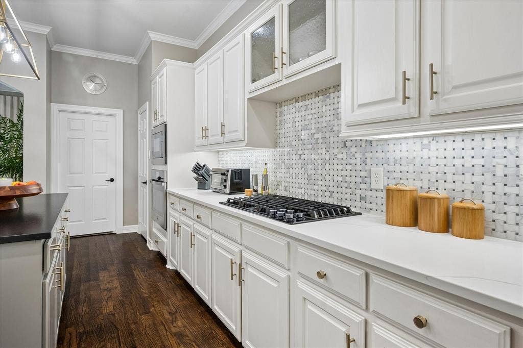 7525 Cedar Elm Drive, Irving, TX 75063 White cabinetry with gold-tone hardware, gas cooktop, patterned tile backsplash, dark wood-finish flooring, and white countertops