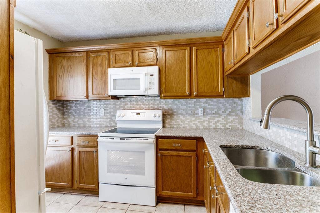 238 Samuel Boulevard, #1T, Coppell, TX 75019 Wood-finish cabinetry, speckled countertop, tile backsplash, stainless steel double basin sink, and an integrated white range