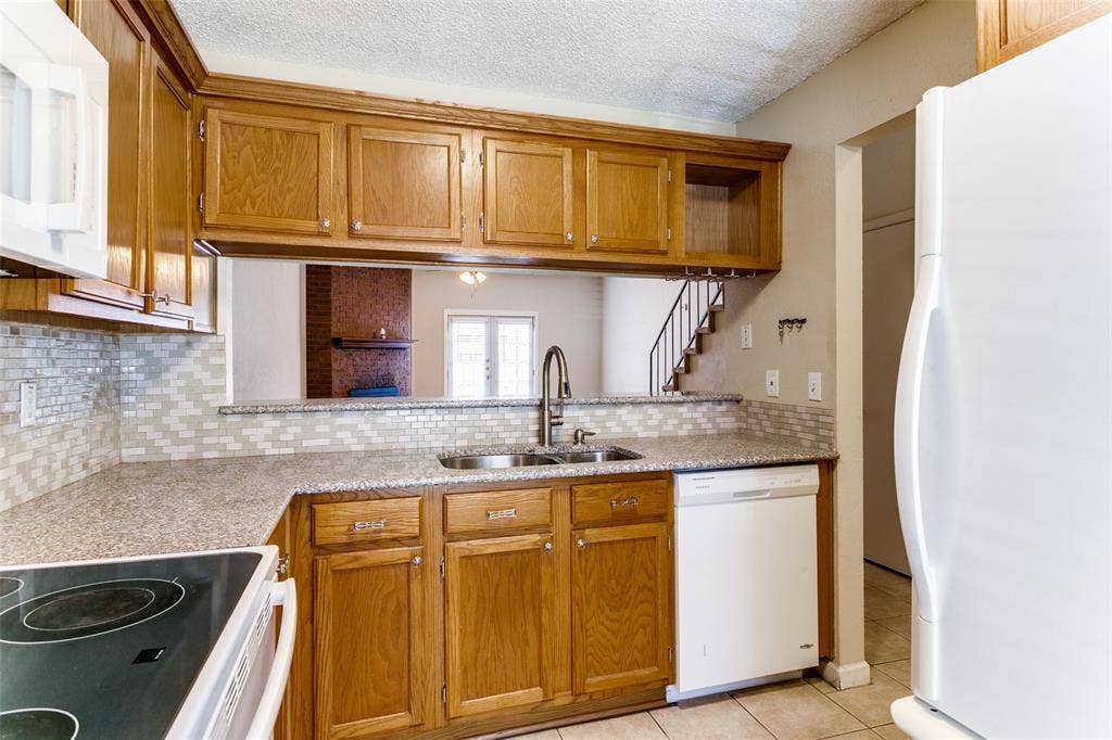 238 Samuel Boulevard, #1T, Coppell, TX 75019 Kitchen featuring wood cabinetry, stone-finish countertops, subway tile backsplash, and stainless steel sink