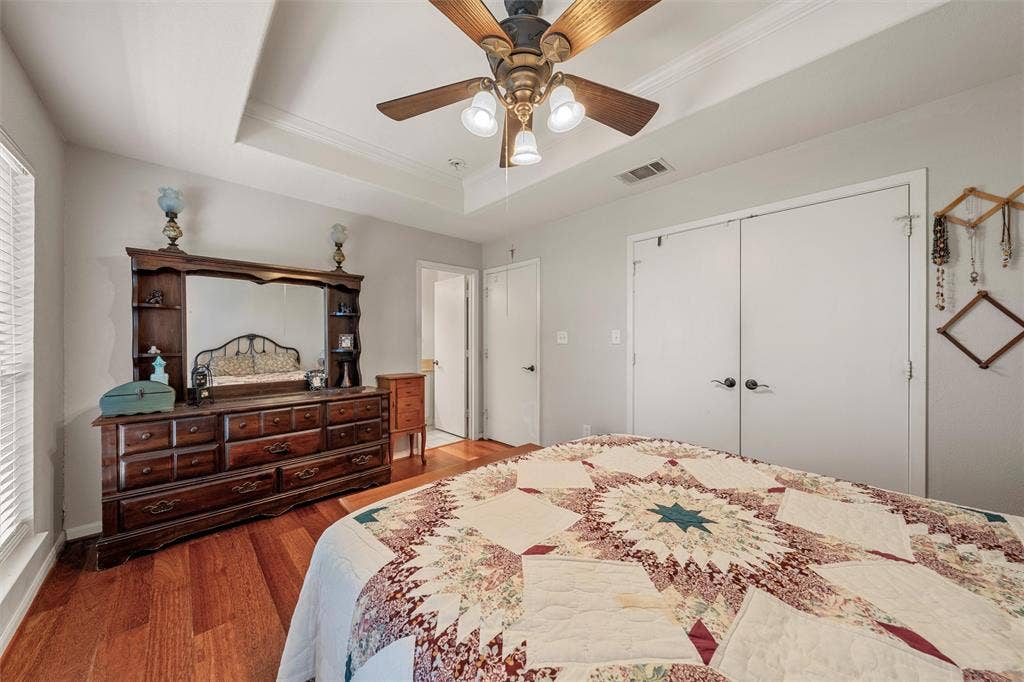 Hardwood flooring, tray ceiling with crown molding, ceiling fan, and two panel closet doors