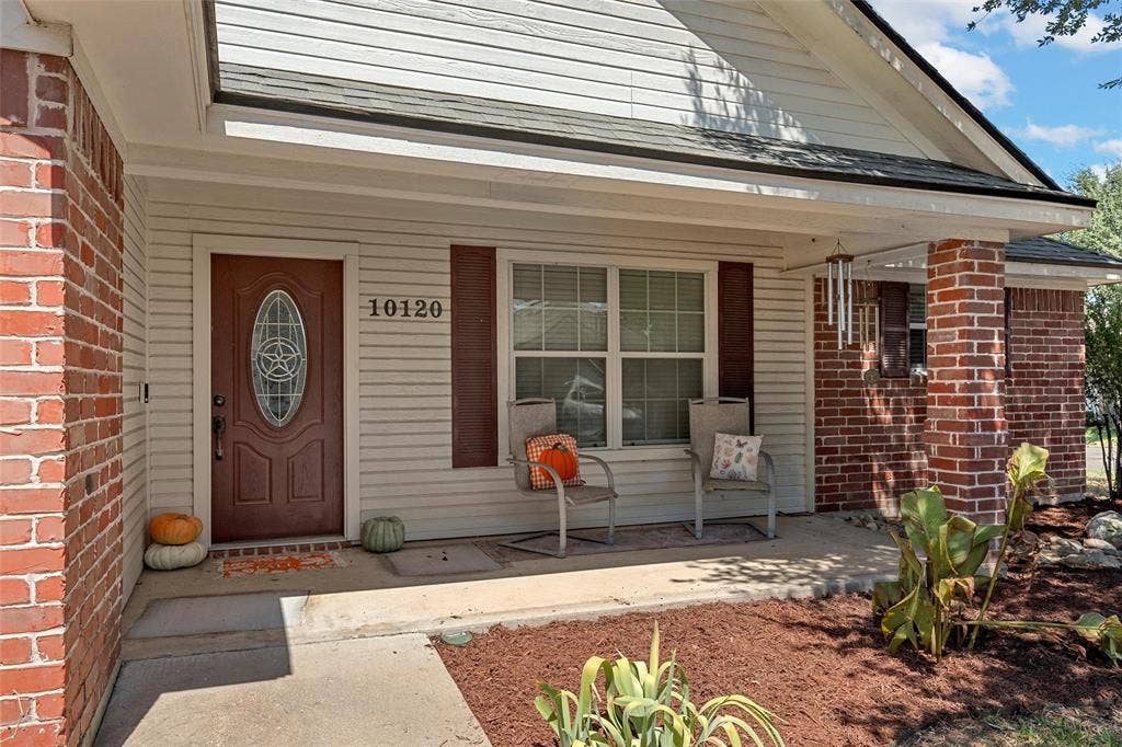 Brick and siding exterior with a covered porch, featuring a substantial entryway and a window with functional shutters
