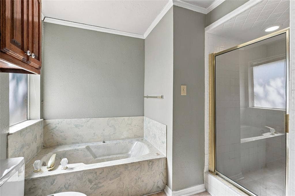 1309 Oxford Lane, Denton, TX 76209 Built-in soaking tub with a stone-finish surround, glass-enclosed shower, wall-mounted towel bar, and wood-finish cabinetry